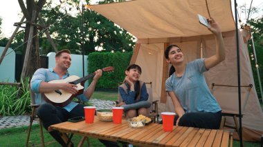 Aile birlikte kamp yapıyor. Baba gitar çalar, anne kız selfie çeker. Ebeveynler, genç nesil arasında iletişim kurmak ve zaman geçirmek için açık hava kamp faaliyetlerini kullanırlar. Uyumsuzluk.