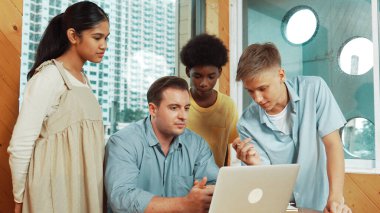 Öğretmen dizüstü bilgisayara bakarken liseli çocuk proje sunuyor. Çeşitli öğrencilerden oluşan bir grup ayakta duruyor ve planı açıklarken akıllı eğitmen de dinliyor ve tavsiye veriyor. Takım çalışması konsepti. Öğretim.