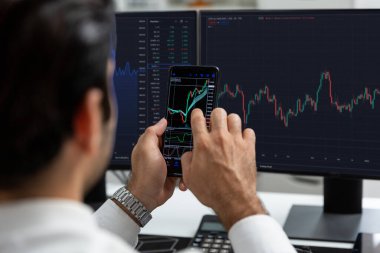 Akıllı telefondan akıllı telefon arayan tüccar işadamı, bilgisayardaki dinamik borsa yatırım ekranını analiz ediyor ve modern merkez ofisteki en kârlı finansal teknoloji pazarına yatırım yapıyor. Tahmin et..