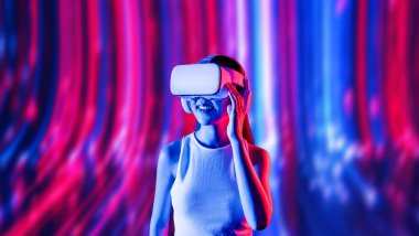 Zeki bir kadın, metaevreni birbirine bağlayan VR kulaklık takan neon ışıklarla çevrili duruyor. Gelecekteki siber uzay topluluğu teknolojisi. Uzaklara bakan zarif bir kadın ve tatmin edici bir şekilde gülümsüyor. Halüsinasyon.