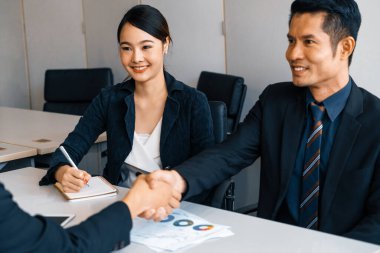 İş adamları konsepti kabul ediyor. Asyalı iş adamı ofis toplantı odasında başka bir iş adamıyla tokalaşıyor. Genç Asyalı sekreter onun yanında oturuyor. uds