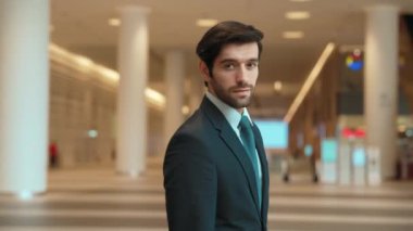 Profesyonel bir iş adamı kolları bağlıyken arkasını döner. Kafkasyalı mutlu yatırımcı, arka planı bulanık bir şekilde koridorda kollarını kavuştururken kameraya özgüvenle bakıyor. Portre. Sevinçli..