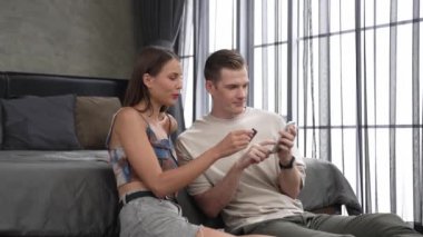 Genç çift, kredi kartıyla ödemek için internet üzerinden ödeme uygulaması ve dijital cüzdan kullanarak yatak odasında oturuyor. Mobil internet üzerinden alışveriş ve modern alımlar. Düzenle