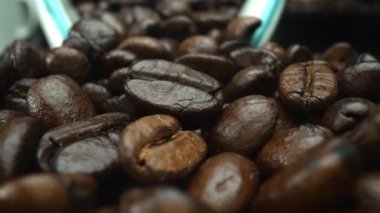 Makro kahve çekirdekleri kamerayla kaşığa saçılıyor. Beyaz kaşık kepçesiyle kahverengi kahve çekirdeklerini kapayın ve siyah arkaplanla dağılın. Kafein enerji içeceği konsepti. Pabulum.