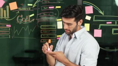 Cam duvara yapışkan notlar yapıştırırken günlük kıyafet yazma fikri içinde profesyonel bir işadamı. Yapışkan notları ve beyin fırtınası fikrini kullanarak zeki bir yönetici. İş için. İzleme