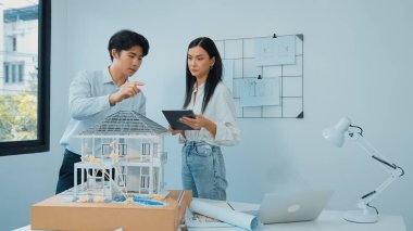 Güzel, genç, beyaz bir proje yöneticisi Asyalı mühendise, mühendislik masasında ev modelini ölçerken tablet kullanarak bina detaylarını anlattı. Tertemiz.