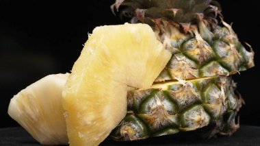 Taze ananaslı ve ayrı siyah arkaplanlı bir ananas dilimli videoyu kapat. Kaba ve balmumu kabuğu, dikenli yeşil yapraklardan bir taç, yemek fotoğrafçılığı. Geliştirilebilir.