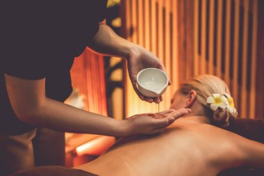 Masör elleri kadının sırtına aroma yağı döküyor. Masözler lüks otellerdeki kaplıca salonundaki müşteriler için yağ masajı prosedürü hazırlıyorlar. Aroma yağı vücut masajı konsepti. Sessiz.