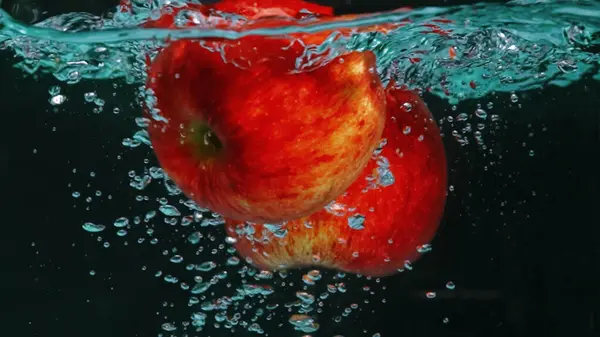 stock image A close up of a fresh vibrant red tomato floating in clear water with black background. Macrography of organic apple falling and dropping in to splashing cool water. Freshness concept. Pabulum.