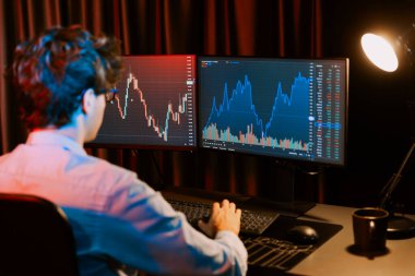 Genç yatırımcı borsa grafiğindeki iki ekran üzerindeki dinamik döviz kuruna odaklanan borsa simsarı, geceleri kahve fincanı olan neon ışıklı modern ofiste, finansal verileri analiz ediyor. Toplayıcı.