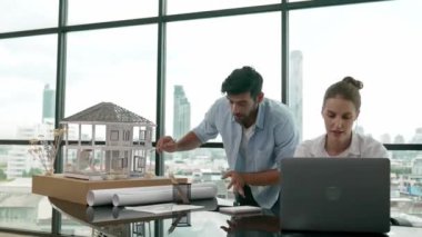 Akıllı mimar mühendis ev modelini incelerken meslektaşı da laptop analiz verilerini kullanıyor. Modern ofisteki ev modeli inşaatında profesyonel tasarımcı takımı birlikte çalışıyor. İzleme