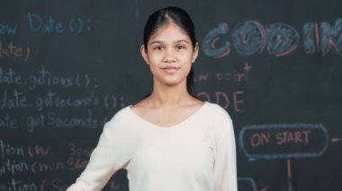 Genç öğrenci başarılı planını kutlarken kolunu kaldırdı. Mühendislik koduyla karatahtaya bakarken kameraya bakan mutlu genç, STEM sınıfında yazılı. Öğretim