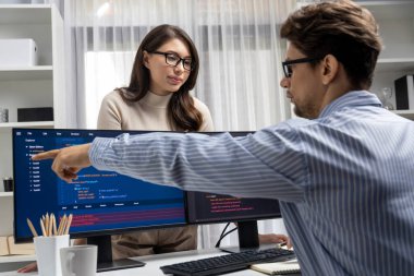Masada çalışan erkek programcının karşısında duran kadın meslektaşım iki bilgisayar ekranında kodlama web sitesi yazılım sistemi projesini tartışmak için tam yığın veri dizaynı ile karşılaştırıyor. Varsayım.