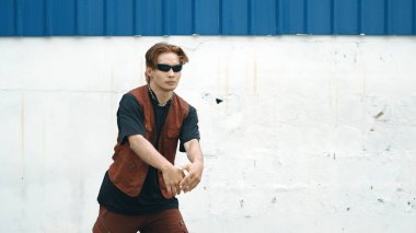 Beyaz arka planda break dans pratiği yapan yakışıklı bir sokak dansçısı. Hip hop tarzı giyinen sporcu, mavi arka planlı bir sokakta müzik eşliğinde ayak sesleri çıkarıyor. Açık hava sporu 2024 hiphop..