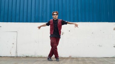 Beyaz arka planda break dans pratiği yapan yakışıklı bir sokak dansçısı. Hip hop tarzı giyinen sporcu, mavi arka planlı bir sokakta müzik eşliğinde ayak sesleri çıkarıyor. Açık hava sporu 2024 hiphop..