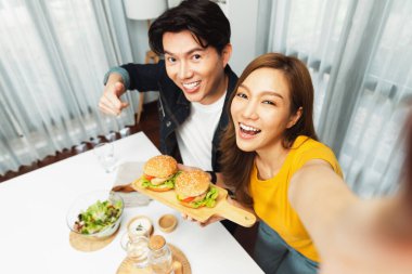 Gülümseyen ev sahibi aşçıların akıllı telefonuyla fotoğraf çekerken üst görüntüsü yemek programında çift hamburger tutarken sosyal medya kanalında ev yapımı salata tabağıyla kolaylıkla görülebiliyor. İnfobahn.