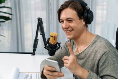 Akıllı yayıncının sunucu kanalı canlı sosyal medya yayını ile akıllı telefon kullanarak dinleyiciyle sohbet ediyor, kulaklık takarak modern ev stüdyosunda video kaydediyor. Bireysel.