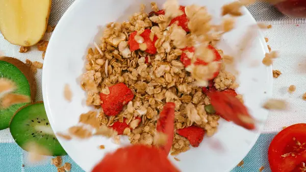 stock image Close up of a healthy cereal and dry strawberry dropping in to bowl. Top down aerial view of bowl with cornflake, dry fruit with blue and white napkin. Macrography. Slow motion. Breakfast. Pabulum.