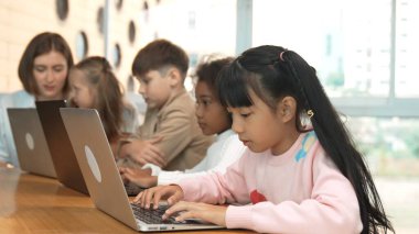 Smart asian girl working on laptop and turn head to doing ok or okay at camera. Diverse children coding or programing engineering code or prompt by using computer in STEM technology class. Erudition. clipart