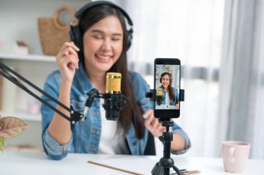 Asyalı sunucu canlı yayında canlı yayında canlı yayında sosyal medyada kulaklık takarak konuşuyor. Dinleyicileri modern stüdyoda koçluk yaparak selamlıyor. Taktik.