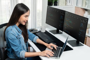 IT geliştiricisinde gülümseyen genç Asyalı dizüstü bilgisayarında kodlama programı verileriyle kotlu tişört giyerek çevrimiçi bilgi yazıyor. Güvenlik analizi iki ekran ile çevrili. Taktik.