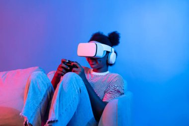 3D hologram ekranında VR kontrol çubuğu takan gülümseyen Afrikalı Amerikalı oyuncu dijital fütüristik teknoloji metaevren dünyasını birbirine bağlayan izole edilmiş neon ışığı kullanıyor. Entrika.