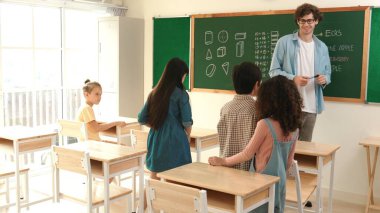 Çeşitli ilkokul öğrencileri öğretmenleri çocuğa bakarken sınıfta yürüyorlar. Profesyonel eğitmen tahtaya çıkıp öğretmenlik yapmaya hazırlanırken sevimli çocuklar sınıfa katılıyor. Pedagoji.