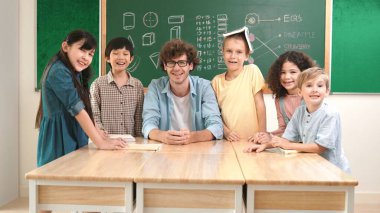 Profesyonel Kafkas öğretmeni ve çeşitli öğrenciler kameraya bakarken mutlu çocuk başparmak gösteriyor. Sınıfın önünde dururken gülümseyen bir grup çok kültürlü çocuk. Eğitim. Pedagoji.