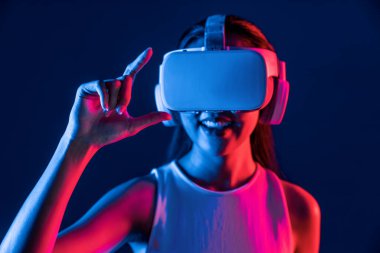 Etrafı neon ışıklı kulaklıklarla çevrili bir kadın metaevreni bağlayan VR kulaklık takıyor, fütüristik siber uzay topluluk teknolojisi yayıyor, işaret ve başparmak ile sanal nesne etkileşimi kuruyor. Halüsinasyon.