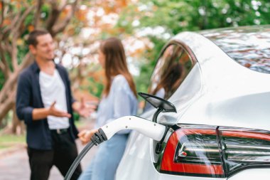 Sonbahar gezisi sırasında sonbahar ormanı EV arabasında elektrikli araba için şarj olan sevimli genç çift. Sonbahar tatilinde çevre dostu seyahat. Yükselt