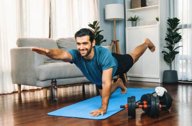 Spor giyimli esnek ve becerikli bir adam evde egzersiz paspası üzerinde meditasyon pozisyonunda yoga yapıyor. Huzurlu ve huzurlu bir yoga yaşam tarzı..