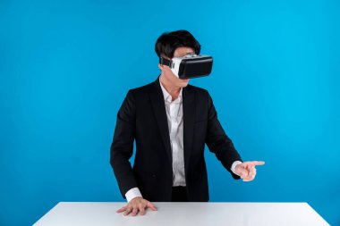 Asyalı iş adamı, sanal gerçekliği mavi telif uzayında ileri teknoloji yenilik teknolojisinde hologram nesnesini masada tutmak için VR ile bağlantı kurmaya çalışıyor. Entrika.