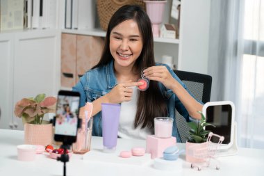 Genç, güzel Asyalı makyaj fırçası yanak testi koleksiyonunu pastel renkle inceliyor. Sosyal medyada akıllı telefonu tanıtmak için pembe ile ışıltılı bir ruh hali sergiliyor. Taktik.
