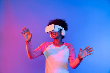Genç Afrikalı, mavi pembe neon aydınlatma grafikli dijital yenilik 3 boyutlu hologram gramında veri öğrenme uygulaması ile metaevren boyunca VR gözlük takıyor. Entrika.