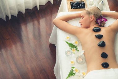 Lüks tatil beldesindeki kaplıca salonunda sıcak taş masajı. Gündüz huzurlu ortam, mutlu kadın müşteri bazalt taşı masajının keyfini çıkarıyor. Sessiz.