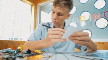 Zeki mutlu çocuk not alırken elektronik alet kullanmayı öğrenir ya da inceler. BTMM sınıfında otururken elektrikli teçhizat üzerine çalışan ve yorum yazan mutlu lise öğrencisi. Öğretim.