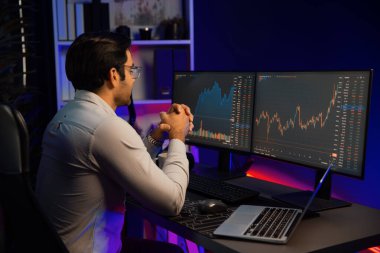 Akıllı tüccar işadamı, karanlık oda gecesinde neon ışıklı ofisteki arama pazarında yüksek kârla ekranda bilgisayar ve bilgisayar üzerinde dinamik borsa yatırımları üzerinde yoğunlaşıyor. Tahmin et..