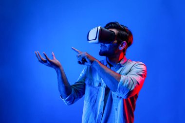 Sanal gerçeklik gözlüklü, sanal gerçeklikte hologram görüntüsü olan beyaz, zeki bir adam. Neon ışıklı arka planda gözlük ve kulaklık kullanarak bakıp işaret eden mutlu bir insan. Teknoloji. Sapma.