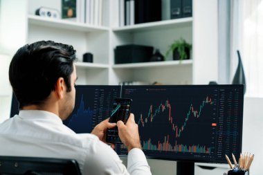 Akıllı telefondan akıllı telefon arayan tüccar işadamı, bilgisayardaki dinamik borsa yatırım ekranını analiz ediyor ve modern merkez ofisteki en kârlı finansal teknoloji pazarına yatırım yapıyor. Tahmin et..