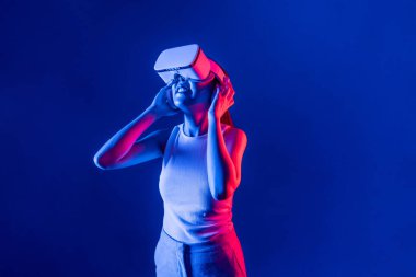 Siberpunk neon ışıklı cihazlarla çevrili zeki bir kadın metaevrene bağlı VR kulaklık takıyor, gelecekçi siber uzay teknolojisi. Zarif bir kadın sanal ortamda yaratılmış gibi görünür. Halüsinasyon.