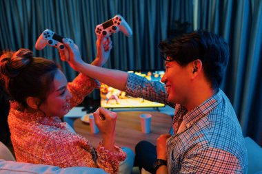 joystick 'in çaprazına sahip bir çift oyuncu arka tarafta televizyon ekranında kazananla kavga oyunu oynuyor modern rahat evinde neon ışıklı oturma odasında kanepesinde oturuyor. İnfobahn.