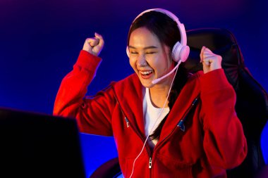 Yüzünde kulaklık renginde kulaklık takan, neon odada online oyun oynayan, Esport meziyetli takım oyuncularına yumruk kaldırarak oynayan güzel Asyalı kız flamasının sunucu kanalı. Taktik.