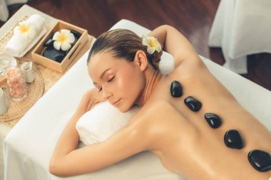 Lüks tatil köyündeki kaplıcalarda sıcak taş masajı. Gün ışığı sükunet ortamında, mutlu kadın müşteri bazalt taş masajından zevk alıyor. Rahatlatıcı bir sıcaklıkla vücudun üzerinde süzülüyor. Sessiz.