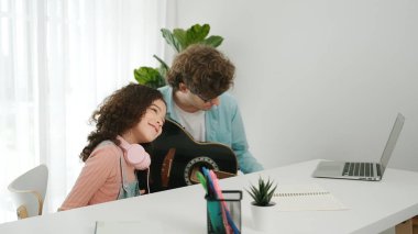 Beyaz bir baba gitar çalar ve müziğe yönelirken Amerikalı kız da akustik şarkı eşliğinde el sallar ve dans eder. Mutlu aile evde birlikte vakit geçirir. Yaratıcı aktivite konsepti. Yaşam tarzı. Pedagoji.