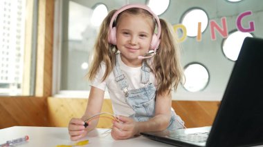 Çalışırken kulaklık takan ve kameraya bakan bir kız. Beyaz çocuk dizüstü bilgisayar, tornavida ve kablolarla bilim deneyi yapıyor. Akıllı online sınıf. Etkinlik.