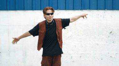 Beyaz arka planda break dans pratiği yapan yakışıklı bir sokak dansçısı. Hip hop tarzı giyinen sporcu, mavi arka planlı bir sokakta müzik eşliğinde ayak sesleri çıkarıyor. Açık hava sporu 2024 hiphop..
