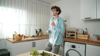 Mutlu baba yemek pişirirken müziğe geçiyor ve modern mutfakta öğle yemeği hazırlıyor. Aktif baba, sebze ve mutfak gereçleri ile çevrili sağlıklı yemek ya da salata yaparken şarkıyla dans ediyor. Pedagoji.