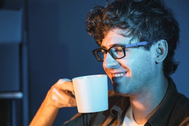 Yaratıcı bir girişim projesinde çalışan genç işadamı, portre görünümlü neon ışıklı modern ofiste bilgisayar başında kahve ya da çay içerken sıcak bir şeyler içiyor. Pazarlama planını düşünüyorum. Toplayıcı.