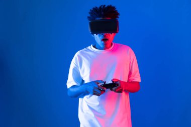 VR kullanan Amerikalı Afrikalı oyun oyuncusu joystick 'i kontrol eden hologram izole edilmiş mavi neon ışıklı duvar ekranı dijital fütüristik teknoloji sanal gerçeklik dünyasına bağlanıyor. Entrika.