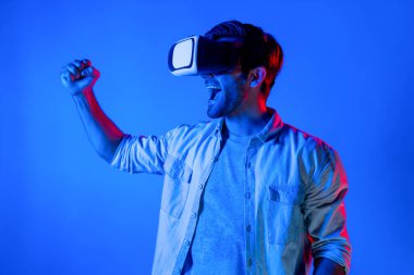 Sanal dünyada spor müsabakalarını izleyen mutlu adam neon ışıklı arka planda VR kulaklık takıyor. Yakışıklı genç, gelecekteki yenilik teknolojisine gözlük kullanarak giriyor. Sapma.